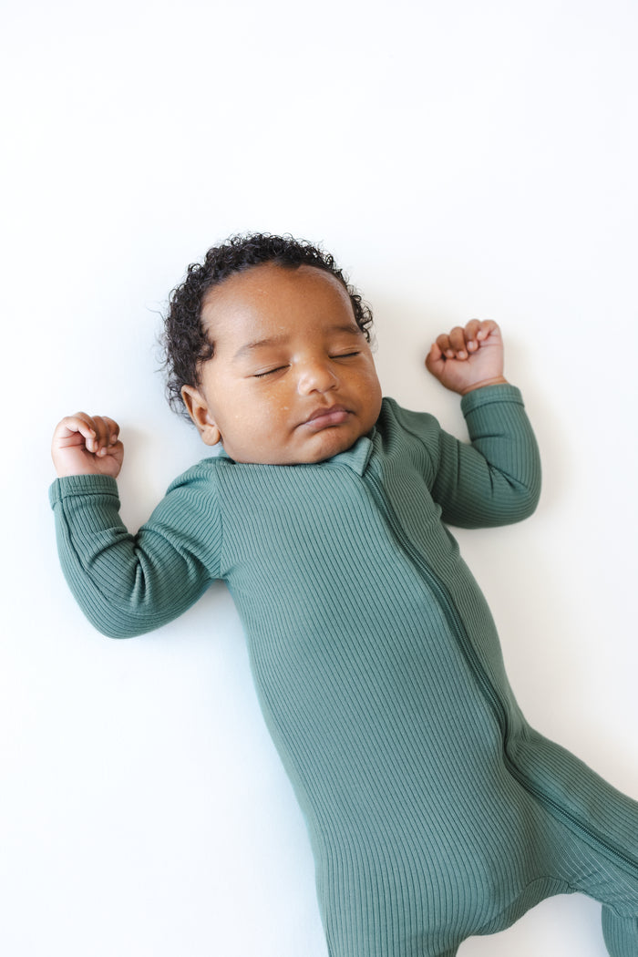 Baby sleeping in Ribbed Zipper Footie in Pine on a white background