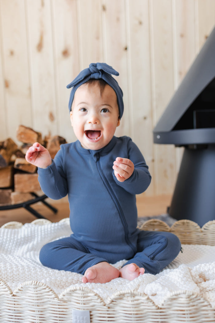 Baby sitting on a basket wearing Ribbed Zipper Romper and Ribbed Headwrap in Oxford