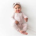 Smiling baby  wearing Kyte Baby Romper in Blush and matching bow headband
