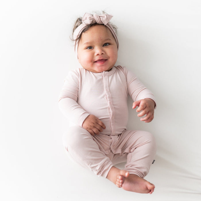 Smiling baby  wearing Kyte Baby Romper in Blush and matching bow headband