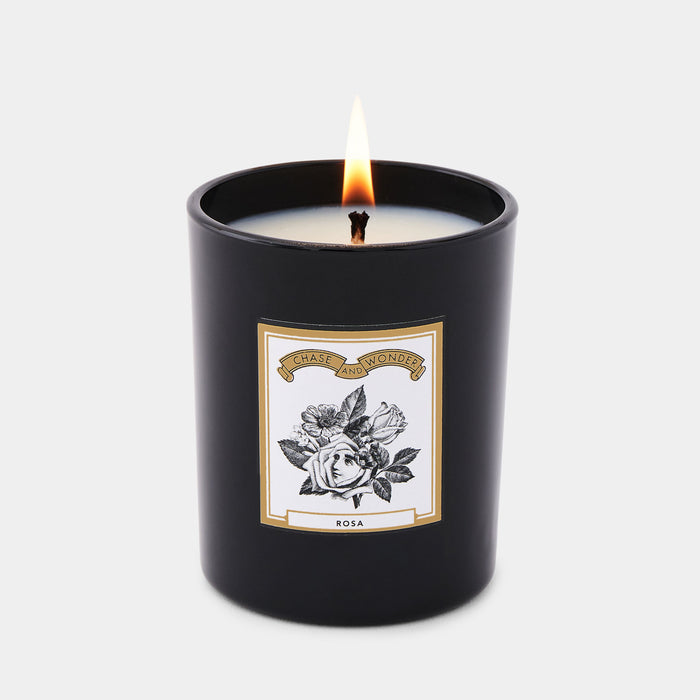 Rosa scented glass candle lit, warm glow through black glass