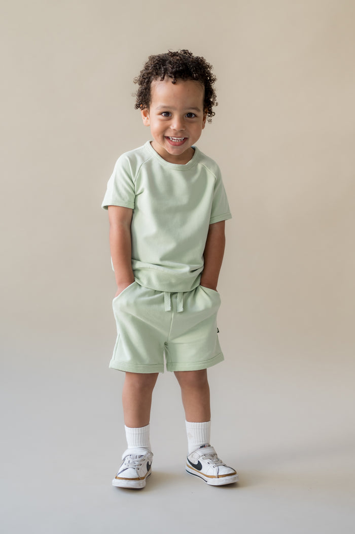 Young boy standing with his hands in the pockets of the Short Sleeve Jogger Set in Basil