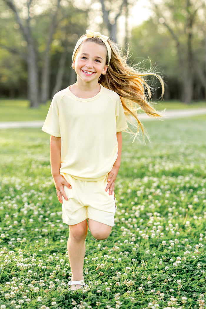 Young girl walking through the grass field wearing the Short Sleeve Jogger Set in Chamomile