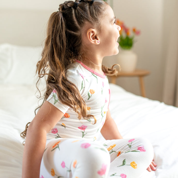 Young girl sitting on the bed wearing the Short Sleeve with Pants Pajamas in Tulip looking off to the side