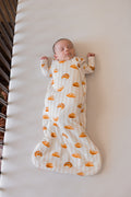 Baby sleeping in Sleep Bag with Croissant 1.0 print in a crib on beige crib sheet.