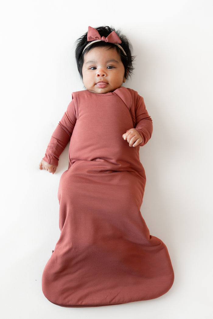 Baby wearing Sleep Bag and Bow headband in Ember 1.0 on a white background