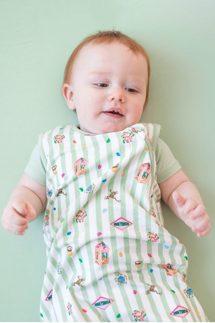 Baby wearing a green and white striped sleep bag with colorful Harry Potter patterns on a green background