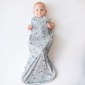 Infant laying on a white surface wearing the Sleep Bag in Mallard