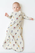 Infant laying on a light neutral surface wearing the Sleep Bag in Mickey Mouse and Friends 0.5 with matching romper
