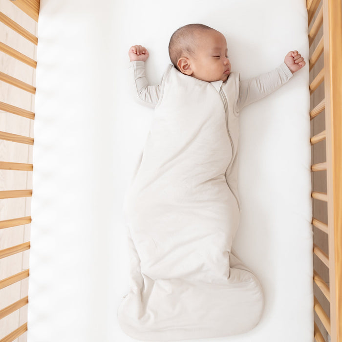 Sleeping baby wearing a Sleep Bag in Oat 1.0 with an Oat long sleeve romper underneath