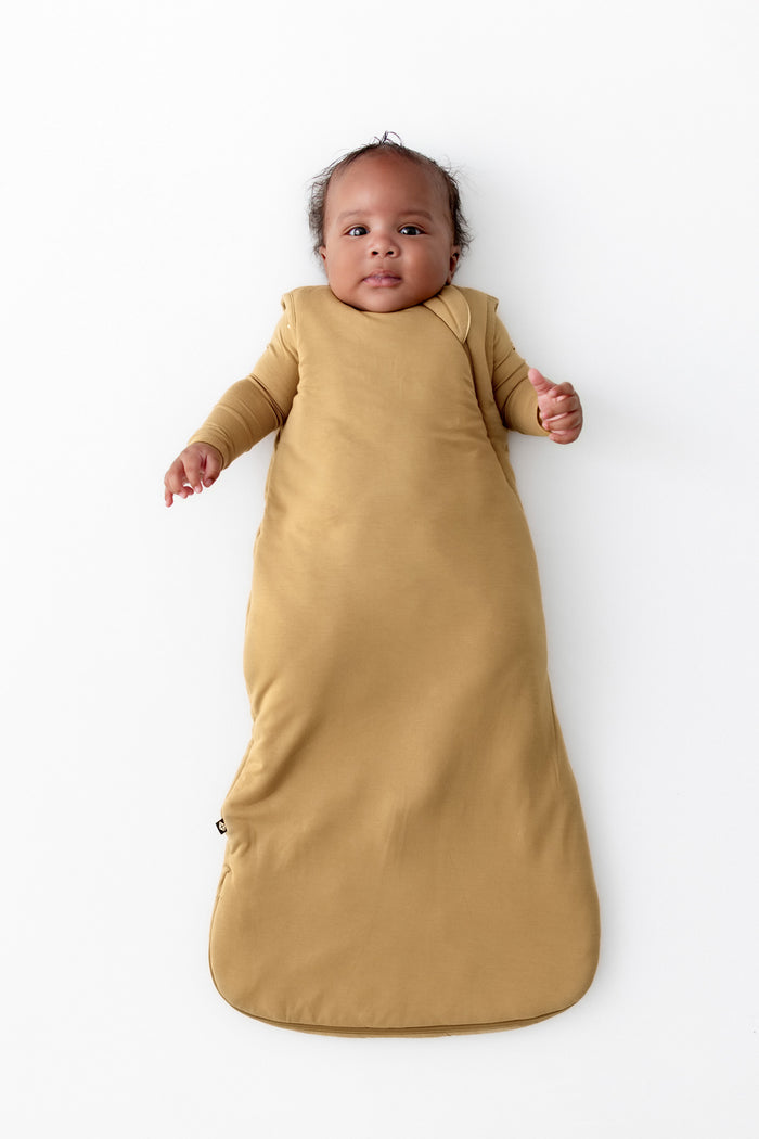 A baby wearing a mustard yellow 2.5 TOG wearable blanket, lying flat on a white background.
