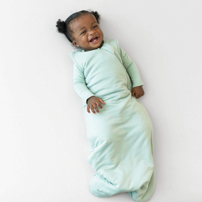 Baby in a cozy sage green wearable balnket on a white background