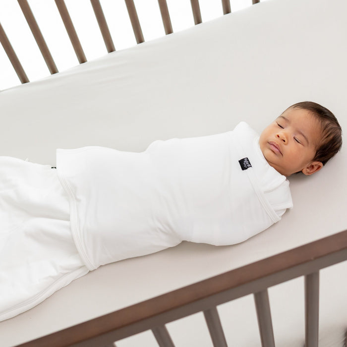 Baby sleeping in a white sleep bag swaddler