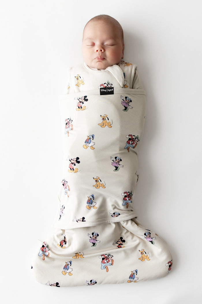 Baby asleep in kyte baby sleep bag swaddler with mickey and friends pattern