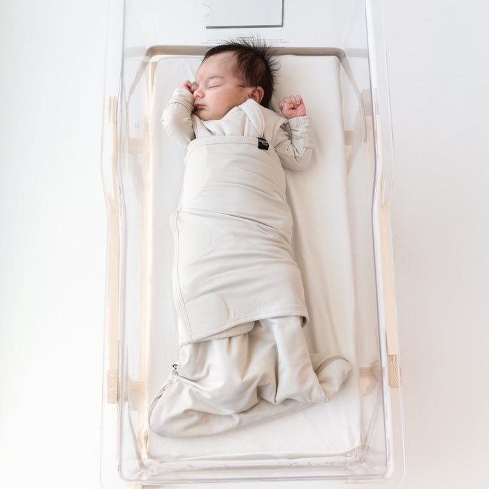 Baby sleeping in bassinet while swaddled in the Sleep Bag Swaddler in Oat 1.0