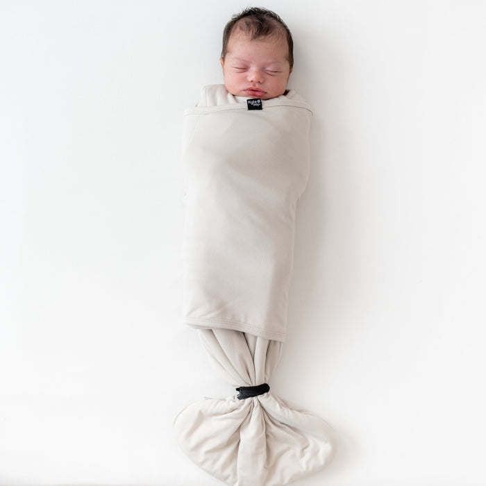 Sleeping baby wearing Kyte Baby Sleep Bag Swaddler in Oat with elastic band at bottom
