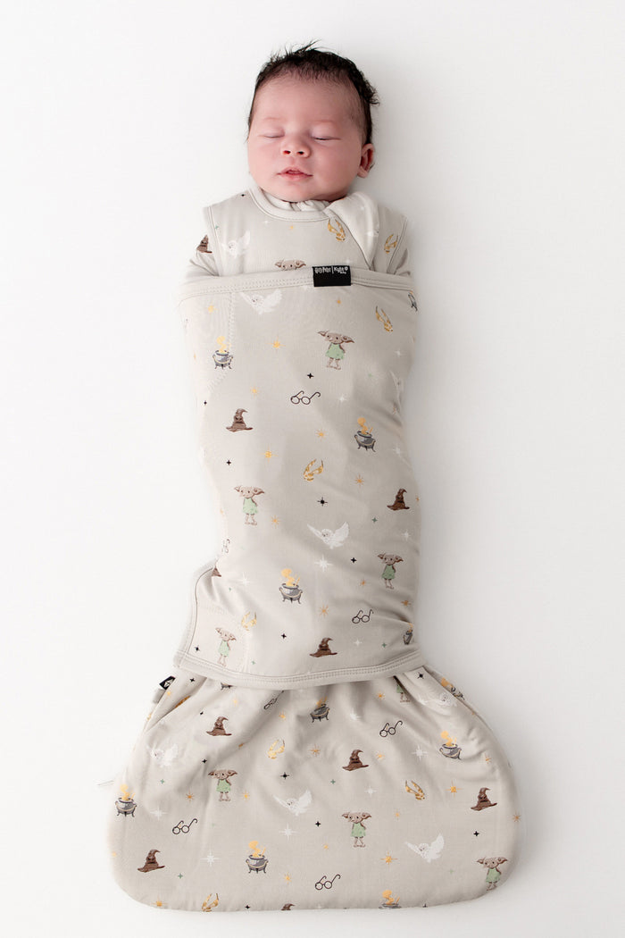 Baby in a Harry Potter patterned cream sleep bag swaddler on a white background