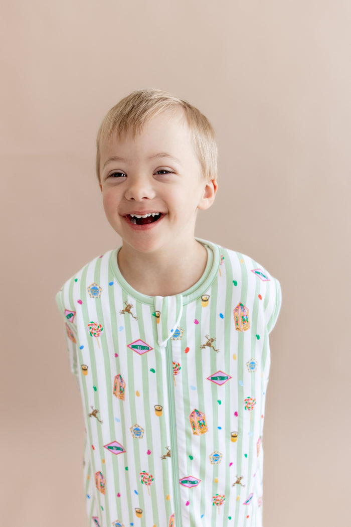 Child in a green and white striped sleep bag walker with colorful Harry Potter patterns on a beige background