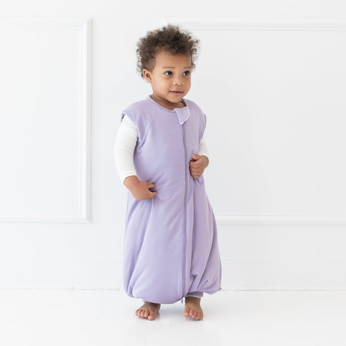 Young model standing looking off to the side wearing the Sleep Bag Walker in Taro 1.0
