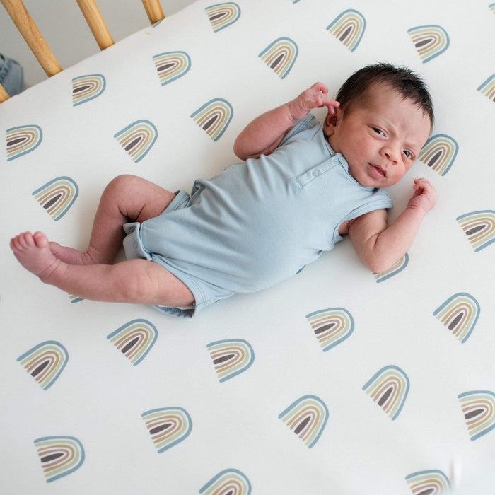 Newborn wearing Kyte Baby Sleeveless infant Bodysuit in Fog while laying in a crib