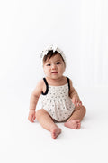 Baby wearing Midnight Polka Dot print Smocked Bubble Romper and bow headband on a white background
