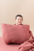 Boy sitting with Standard Pillowcase in Ember and similar color blanket and sheet