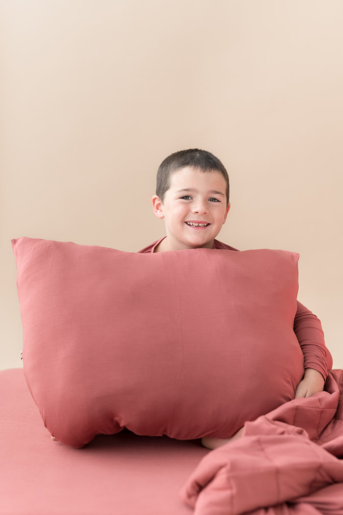 Boy sitting with Standard Pillowcase in Ember and similar color blanket and sheet