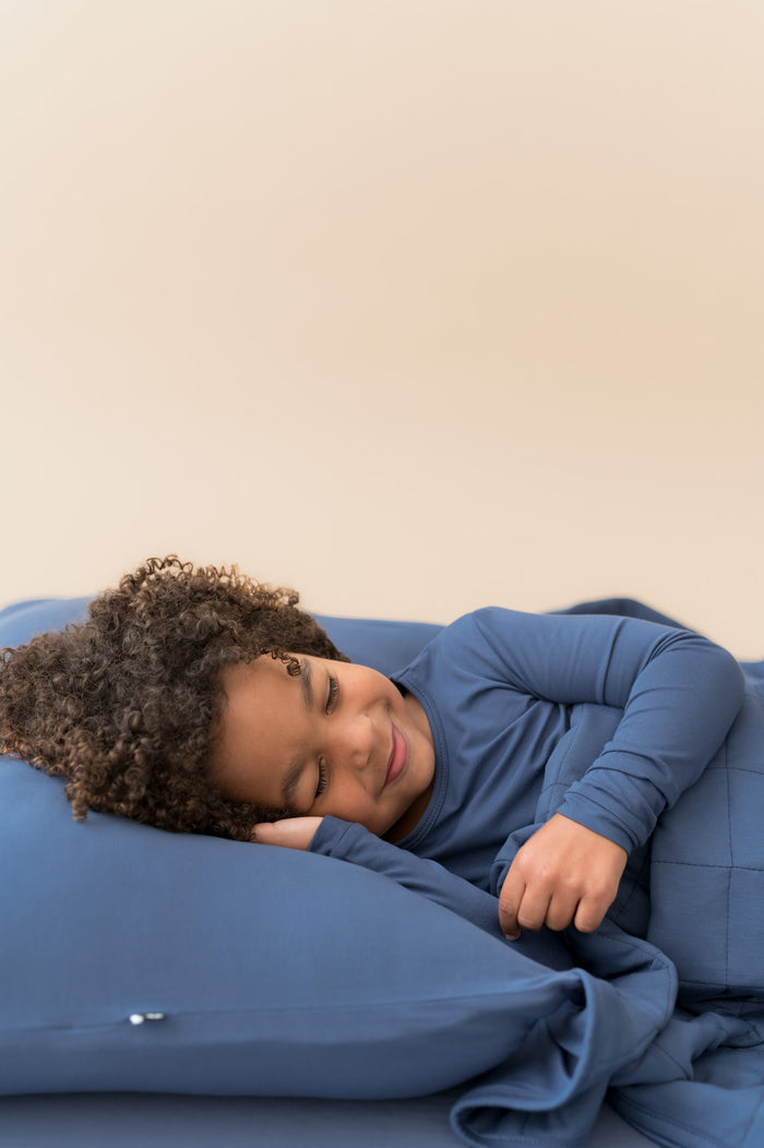 Boy sleeping on Standard Pillowcase in Oxford wearing similar color shirt and covered with Oxford blanket