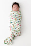 Baby wrapped in a green and white striped Swaddle blanket with colorful Harry Potter patterns on a white background