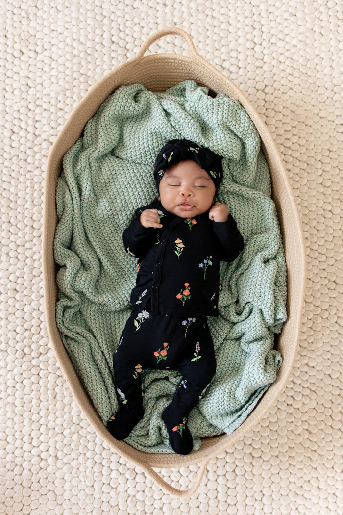 Baby sleeping in a basket wearing Take Me Home Set with Bow in Midnight Wildflower print lying over a green blanket