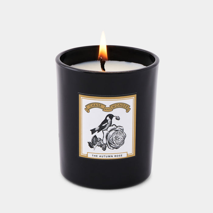 The Autumn Rose scented glass candle lit, warm glow through black glass