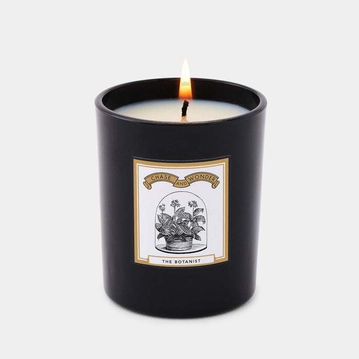 The Botanist scented glass candle lit, warm glow through black glass