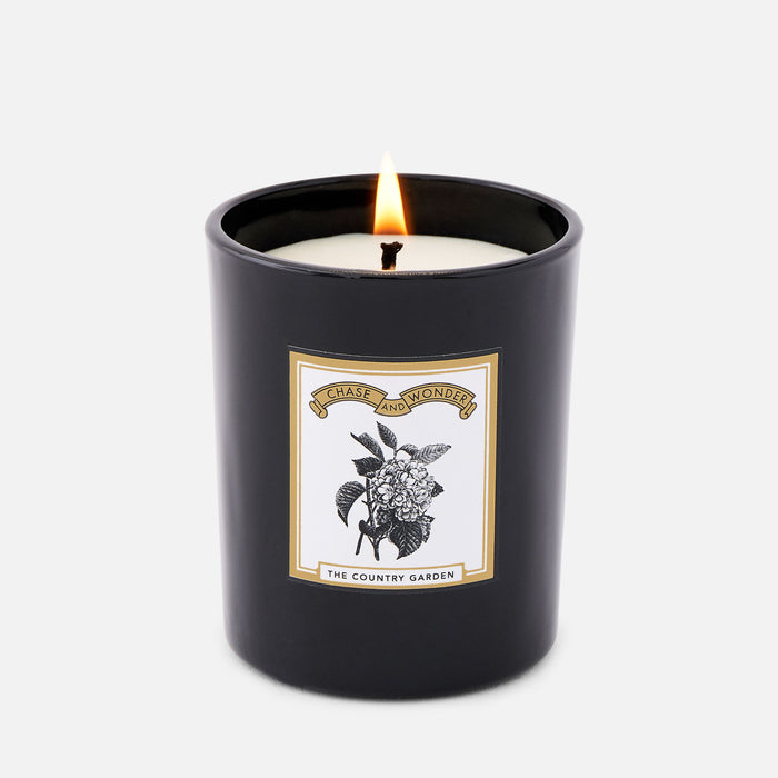 The Country Garden scented glass candle lit, warm glow through black glass