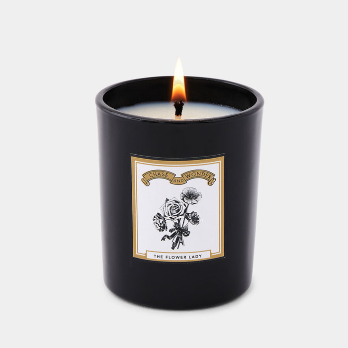 The Flower Lady scented glass candle lit, warm glow through black glass