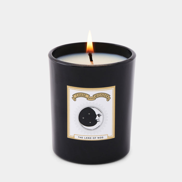 The Land of Nod Luxury scented glass candle lit, warm glow through black glass