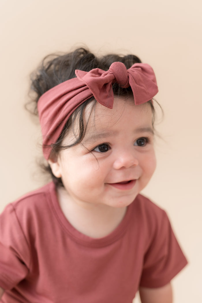 Child wearing Toddler Basic Tee in Ember with similar color knotted bow headband