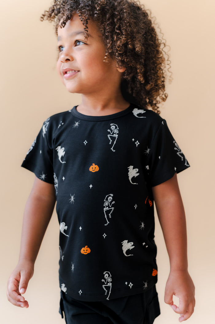 Boy wearing Toddler Basic Tee in Halloween Friends print over black shorts on a beige background