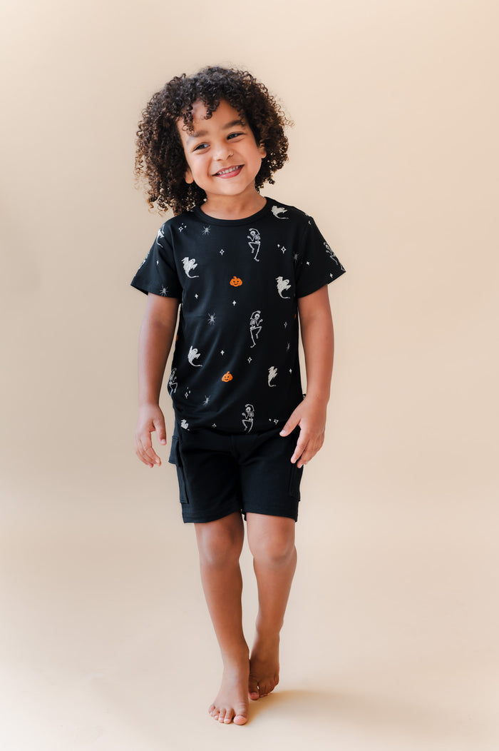 Boy posing in Toddler Basic Tee in Halloween Friends print over black shorts on a beige background