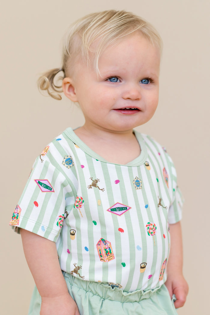 Child wearing a green and white striped Toddler Basic Tee with colorful Harry Potter patterns on a beige background