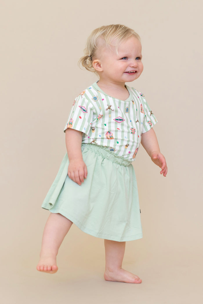 Child wearing a green and white striped Toddler Basic Tee with colorful Harry Potter patterns with a green skort on a beige background