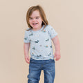 Smiling child wearing the Toddler Basic Tee in Take Off with medium wash jeans