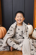 Boy wrapped in a Toddler Blanket in Bats 1.0 print sitting wearing a similar print long sleeve pajama set with pumpkin props all around him