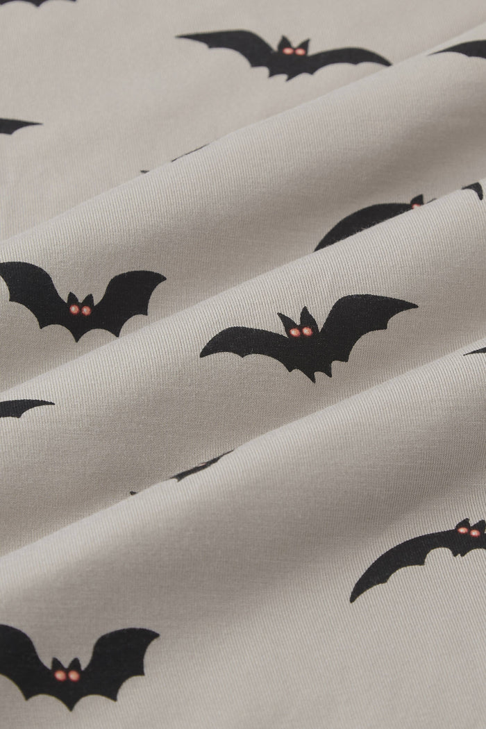 An all-over print featuring the silhouettes of various flying bats with orange eyes over a light tan background color called Khaki.