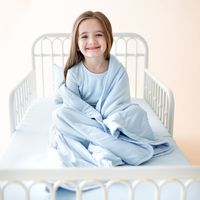 Young girl sitting in bed with the Toddler Blanket in Breeze 1.0 wrapped around her