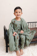 Boy wrapped in Green Toddler Blanket in Groot 1.0 print sitting on a bed wearing a similar print long sleeve pajama set