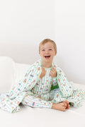 Child sitting on a white bed wrapped in a green and white striped toddler blanket with colorful Harry Potter patterns wearing a similar print long sleeve pajama set