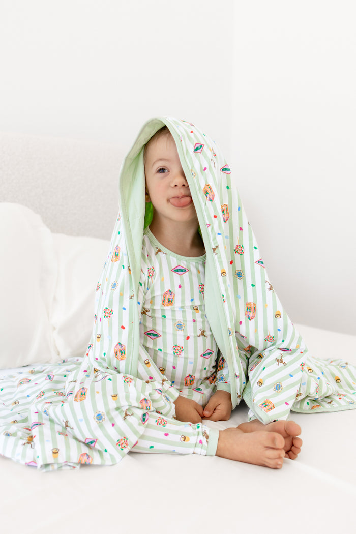 Child sitting on a white bed under in a green and white striped toddler blanket with colorful Harry Potter patterns wearing a similar print long sleeve pajama set