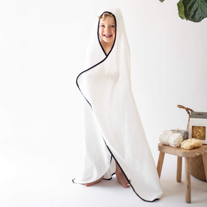 Toddler wrapped in Kyte Baby Hooded Bath Towel in Cloud with Midnight Trim