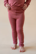 Child wearing Toddler Leggings in Ember on a beige background