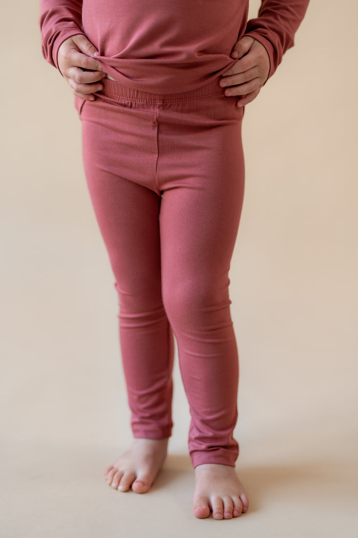 Child wearing Toddler Leggings in Ember on a beige background